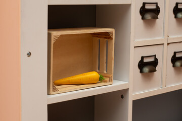 Fresh orange carrot resting in a wooden crate on a shelf, surrounded by white cabinetry, showcasing a minimalist kitchen storage concept with natural elements