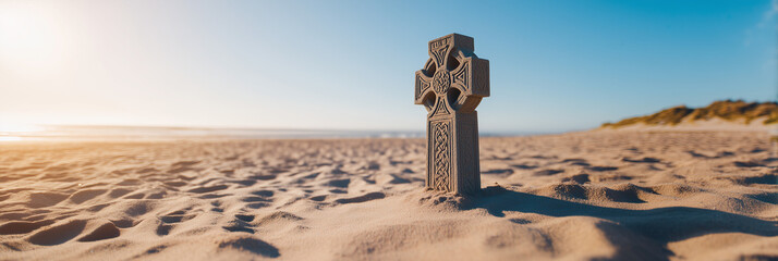 Celtic cross sculpture standing alone on sandy beach against clear blue sky, serene concept of meditation or reflection
