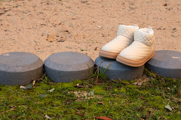 Cozy white quilted boots resting on circular stone pavers surrounded by green grass and sandy ground, showcasing a serene outdoor footwear scene with natural elements