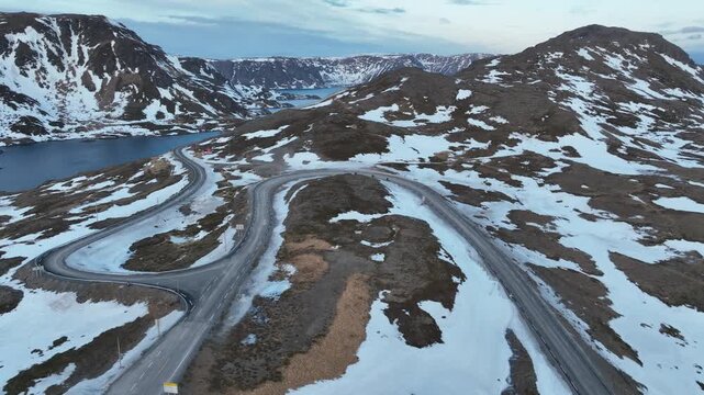 Winding Mountain Road Through Snow Patches and Remote Alpine Landscape. Norway. Motorcyclist on the Road