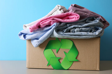 Recycling concept. Various clothes and recycling sign on bright background. Conscious use of clothes