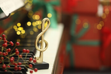 Christmas atmosphere. Golden treble clef and berries on piano against blurred background, closeup with space for text. Bokeh effect