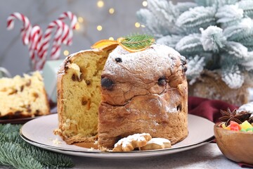 Tasty panettone cake, candied fruits and Christmas decor on grey table against blurred lights, closeup. Bokeh effect