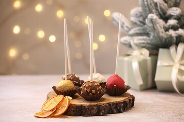 Sweet cake pops, slices of dried orange and Christmas decor on table against blurred lights, closeup. Bokeh effect