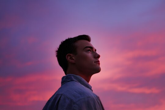 Young man looks up towards colorful sunset sky with clouds