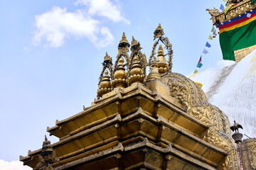 A close view captures the intricate golden details of the Swayambhunath Stupa architecture. Decorative spires and carvings are visible with prayer flags waving in the background