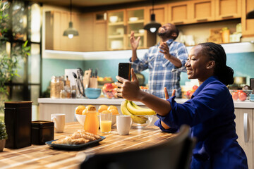 African american woman takes selfies on her smartphone and acting silly, boyfriend laughing at her and enjoying a cute funny moment together on a weekend morning. Relaxation at home.