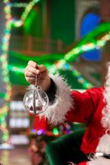 Naklejka premium Close up of entertainer wearing red xmas suit holding Christmas prop, doing festive decorations for holiday season ambiance. Santa Claus using globes to decorate room during December festivities