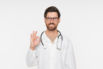 Portrait of doctor, general practitioner, physician, medical professional wearing white uniform coat and stethoscope, posing with okay gesture and smiling isolated on white studio background