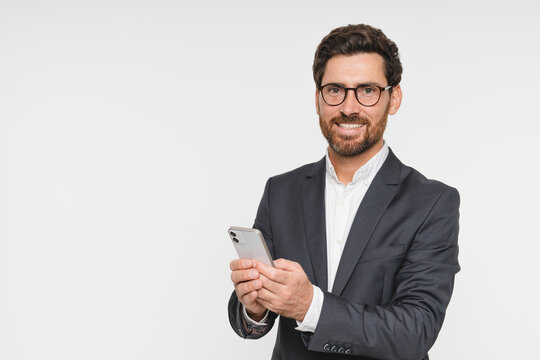 Business man wearing suit using phone cellphone standing isolated on white background. Busy young businessman with smartphone in hands looking at camera, advertising mobile services, copy space