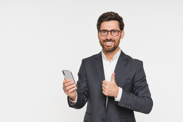 Business man in suit using phone cellphone with thumb up gesture standing isolated white background. Busy businessman with smartphone in hands looking at camera advertising mobile services, copy space