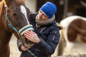Fototapeta premium Woman gently bonding with her horse during winter grooming outdoors