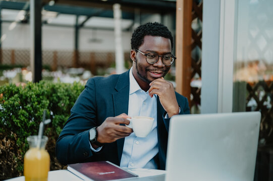 Black businessman drinking coffee working on laptop