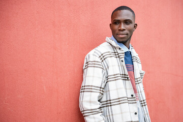 Stylish man in checkered jacket poses against a vibrant coral wall in a trendy urban setting