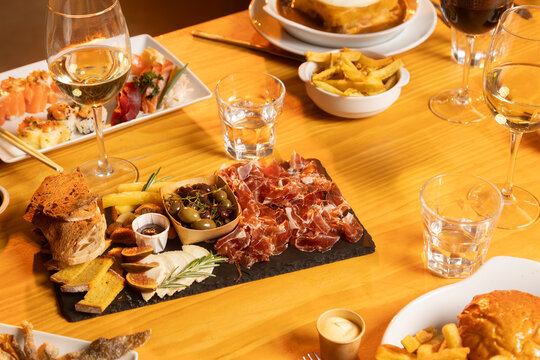 Assorted appetizers and wine on a wooden table, including cured meats, cheese, olives, bread, and various dishes served in a warm restaurant setting.