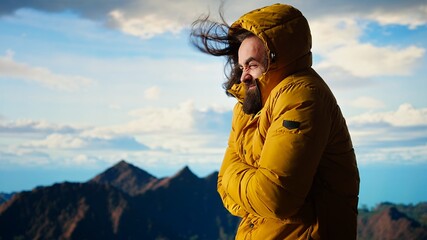 Male nature lover struggling with the cold windy weather on the mountain top, climbing the rocky hills and feeling cold. Young hiker adventure seeker enjoying the scenic landscape. Camera A.