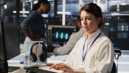 Data center software developer using PC to monitor neural network AI visualization. Woman working in server room using computer to oversee rigs powering machine learning processes, camera A