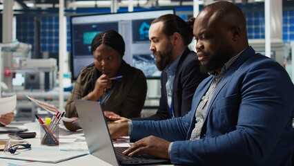 Factory manager developing lucrative business model using laptop, expanding production. Man works on integrating automation technology in industrial plant, looking at equipment on notebook, camera A