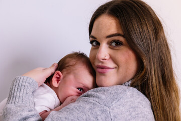 Mother embracing newborn baby at home, feeling joy