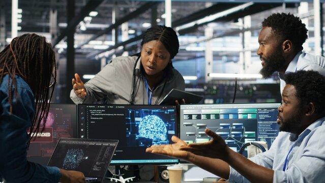 Data center engineer in wheelchair using AI requesting help from coworkers during security breach. Server farm worker with disability aided by colleagues to fight hacker attack stealing data, camera B