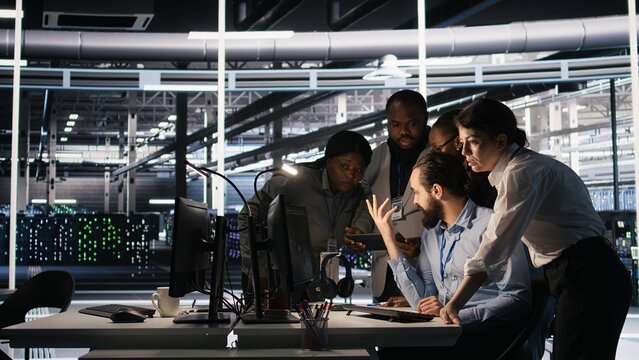 Data center system administrators performing maintenance on supercomputers used for AI processing. Team managing server hub rigs used for deep learning training, looking over business charts, camera A