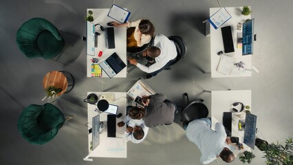 Top down view of employees reviewing charts and diagrams during briefing. Corporate team leads discussions on planning, documentation and report writing to enhance business intel.