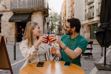 A woman talks to a man while they clink drinks and smile while sitting at a table
