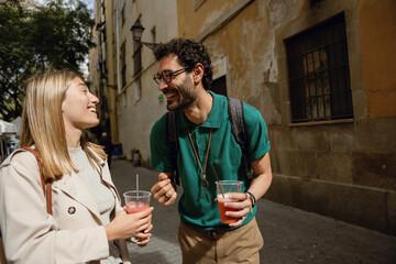 Fototapeta premium Man and woman looking at each other and laughing while walking and holding drinks