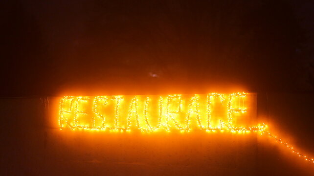 Illuminated lettering spells 'RESTAURANT' against a dark backdrop. Numerous lights form the word. The display is vibrant. A warm glow emanates. The scene appears festive