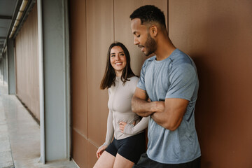 Female athlete smiling and listening to male athlete talking while they stand and lean on a wall