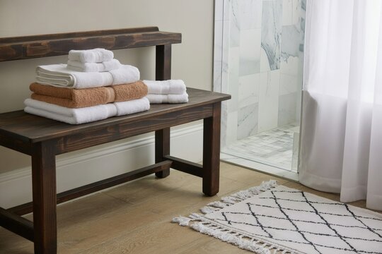 Stacked bath towels on rustic wooden bench near shower