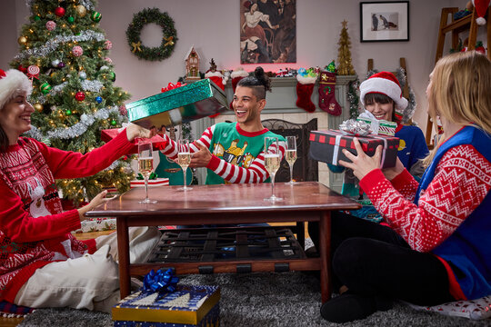Friends exchange gifts in festive sweaters during a cozy Christmas celebration at home