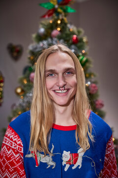 Young man with septum piercing smiling in festive cat sweater by decorated Christmas tree