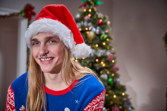 Young man with piercings wearing Santa hat celebrates alternative Christmas with decorated tree