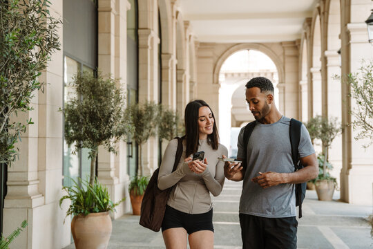 Male and female athletes looking at phone, he showing it while she smiles - Powered by Adobe