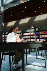 Female student smiling and reading a notebook while holding a pen and sitting on a chair at a desk
