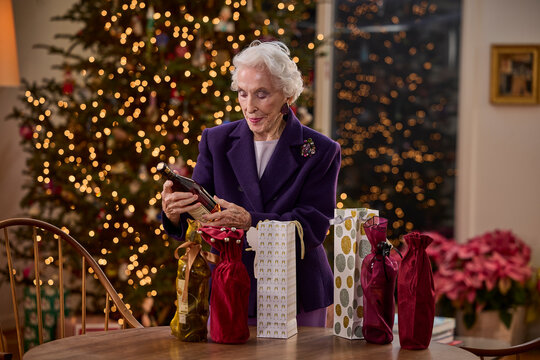 Elderly woman enjoying holiday gift wrapping in a cozy, festive home setting