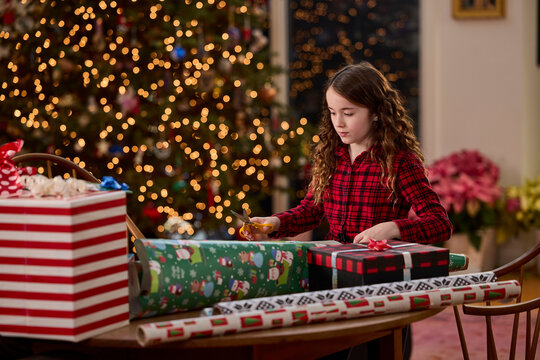 Young girl wrapping christmas gifts by the tree, creating festive holiday memories at home