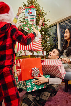 Family celebrates Christmas morning with stacked wrapped presents near decorated tree at home