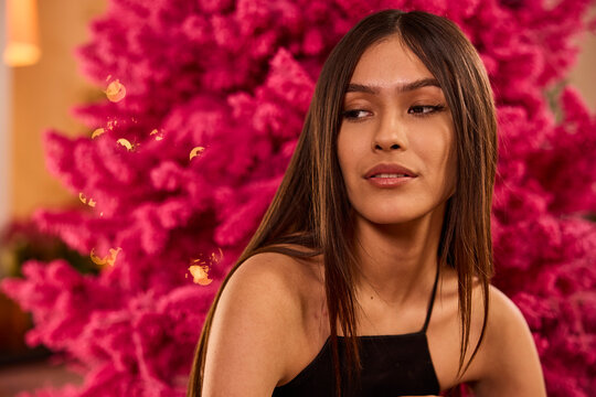 Woman in black dress poses against vibrant pink floral backdrop at elegant event