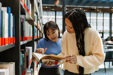 A female student points in surprise at a book held by a female student standing next to her and reading