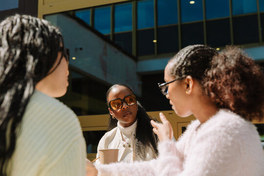 A female student listens to a female student gesturing and talking while another female student next to them listens to her