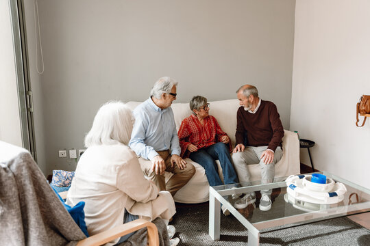 A group of three friends are sitting on a couch and talking while a female friend listens and sits on a chair - Powered by Adobe