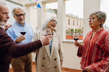 A group of four friends stand and hold glasses while one of them talks and one of them laughs