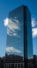 Modern skyscraper reflecting clouds against a vibrant blue sky.