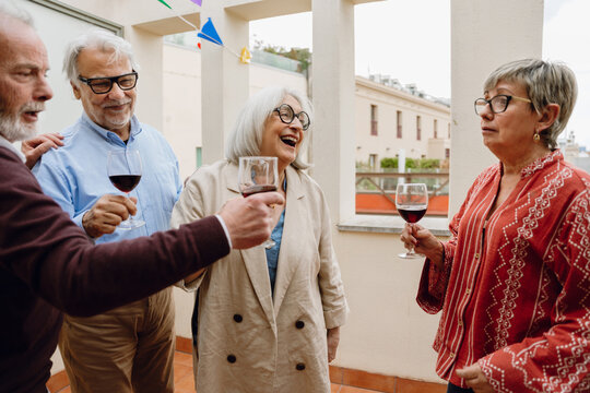 A group of four friends stand and hold glasses while one of them talks and one of them laughs