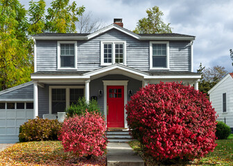 Charming two-story family home with gray siding and bright red door in Brighton, Boston area,...