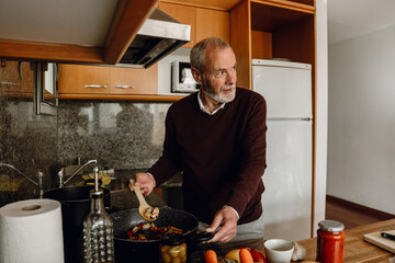 Man holding frying pan and food in spatula while looking away