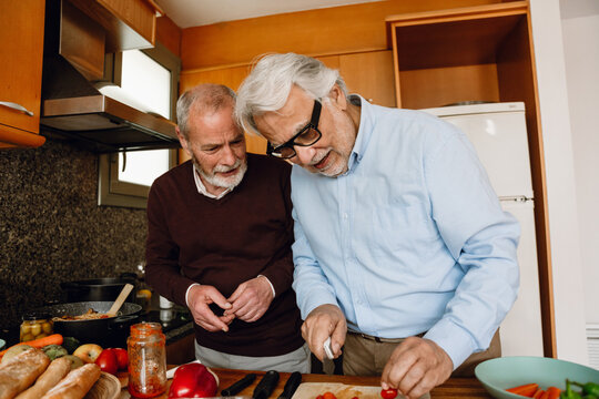 A man is talking to a male friend who is holding a knife while they are standing at a table