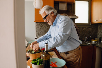 Man smiling and pouring salad into a bowl while standing at the table
